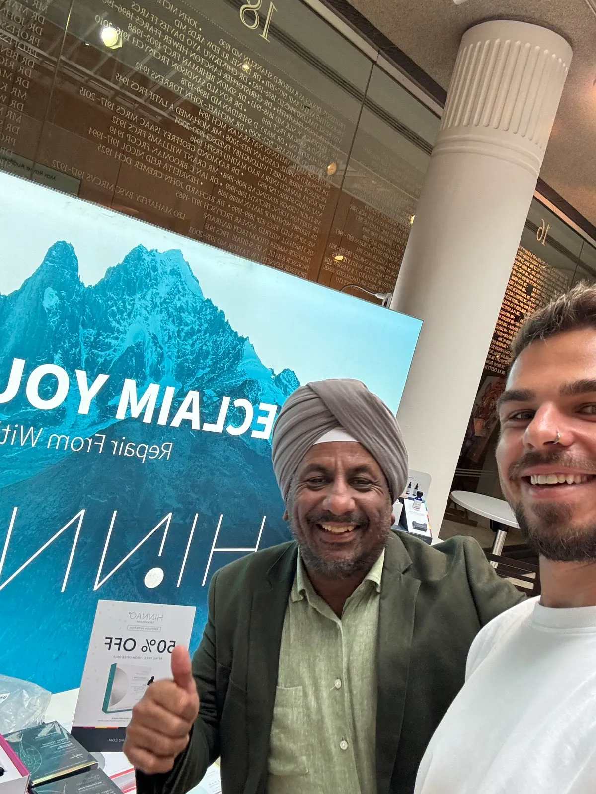 Two attendees smiling together beside the HINNAO display at the Royal Society of Medicine